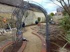 The new sinuous brick path and wirework arch are installed